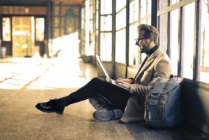 Homme avec son ordinateur portable ouvert dans une gare, assis sur le sol